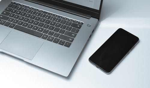 From above of contemporary netbook and cellphone with black screen on white desk