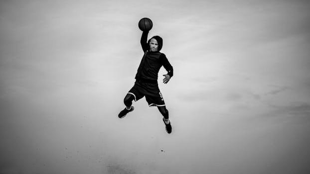 High-flying black and white shot of a man dunking a basketball outdoors.