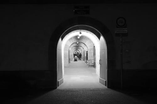 Black and white of aged house with passage and open door illuminated by artificial light