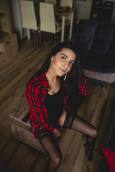 Portrait of a woman in alluring attire sitting indoors, exuding confidence and style.