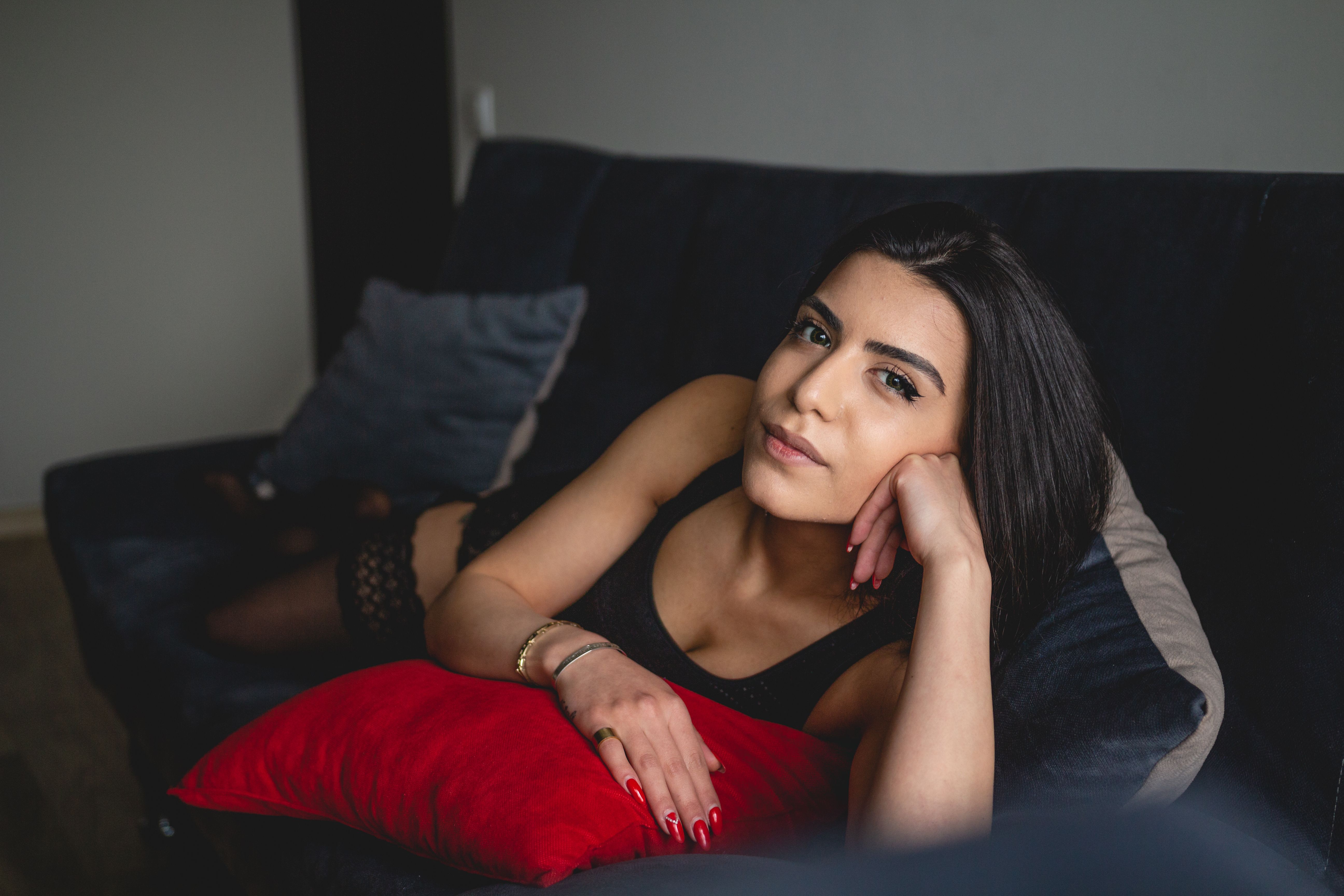 A young woman in black lingerie lying on a couch looking at the camera with a relaxed expression.