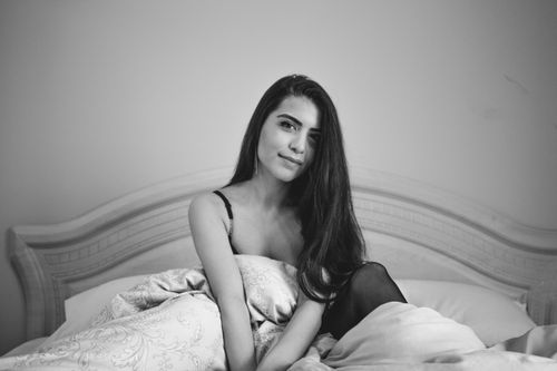 Free A woman with long hair sits gracefully on a bed in a black and white setting, conveying elegance. Stock Photo