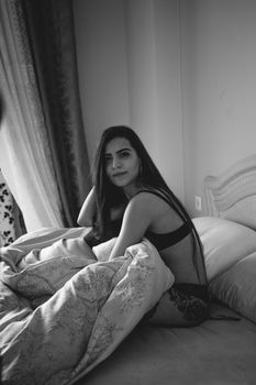 Black and white image of a woman sitting in bed, creating a moody and intimate feel.
