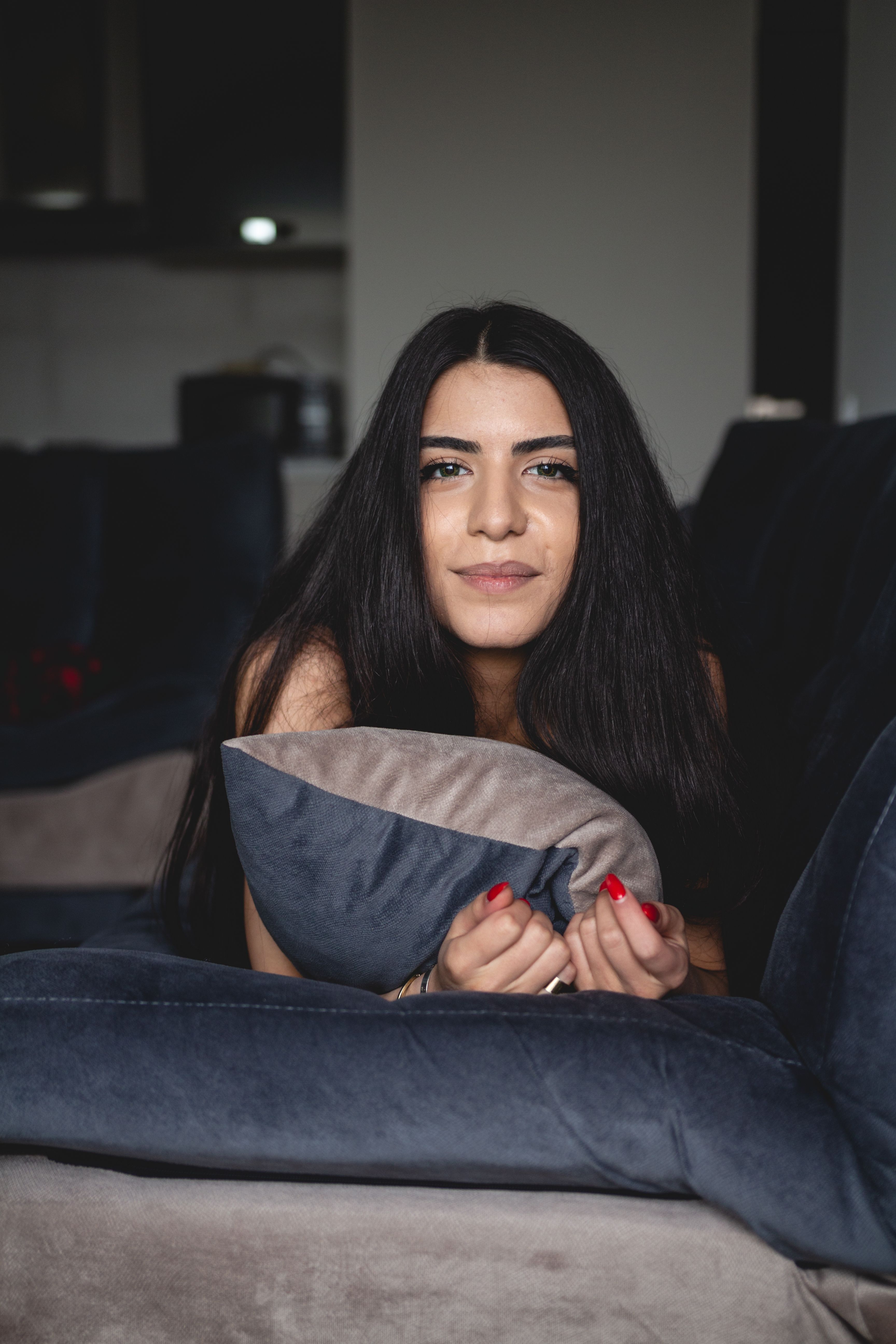 Smiling brunette woman relaxing indoors, leaning on a throw pillow.