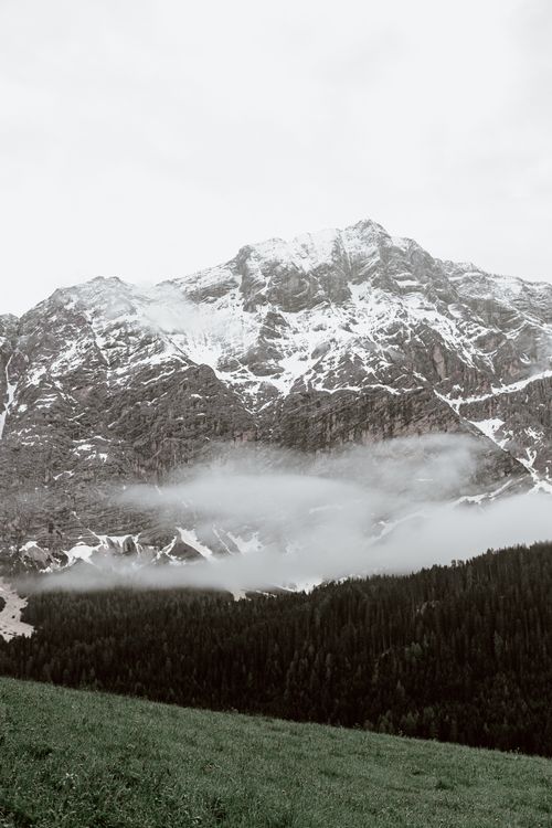 Free Amazing view of majestic mountain covered with snow located near green forest under cloudy sky Stock Photo