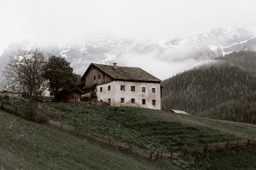 Free Aged house located on grassy valley near green forest trees growing near mountain ridge under cloudy sky Stock Photo