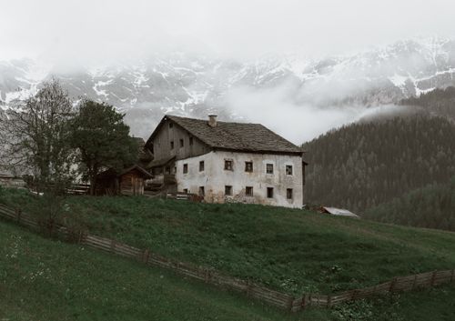 Free Weathered house located on rough grassy terrain near vast forest trees growing near mountain slope covered with snow in cloudy day Stock Photo