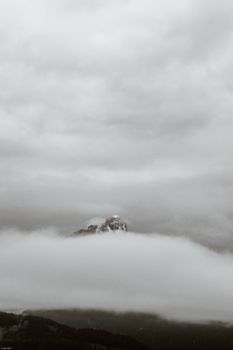 透过浓雾，一座白雪皑皑的山峰在多云的天空下显现，景象颇为壮观