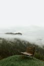 森林附近的山上，木凳旁的风景如画，常绿树木映衬着白天雾气阴沉的天空