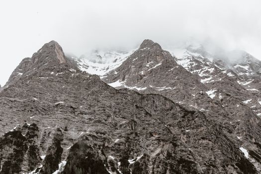 Amazing view of snowy mountain peaks with steep slopes in overcast cloudy weather
