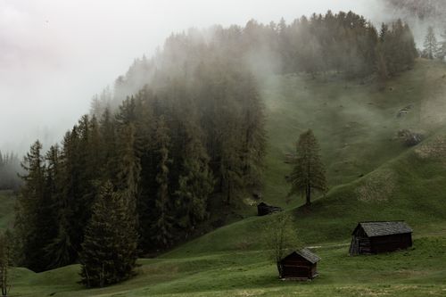 Free Aged small wooden buildings in green valley against foggy hill with green woodland Stock Photo
