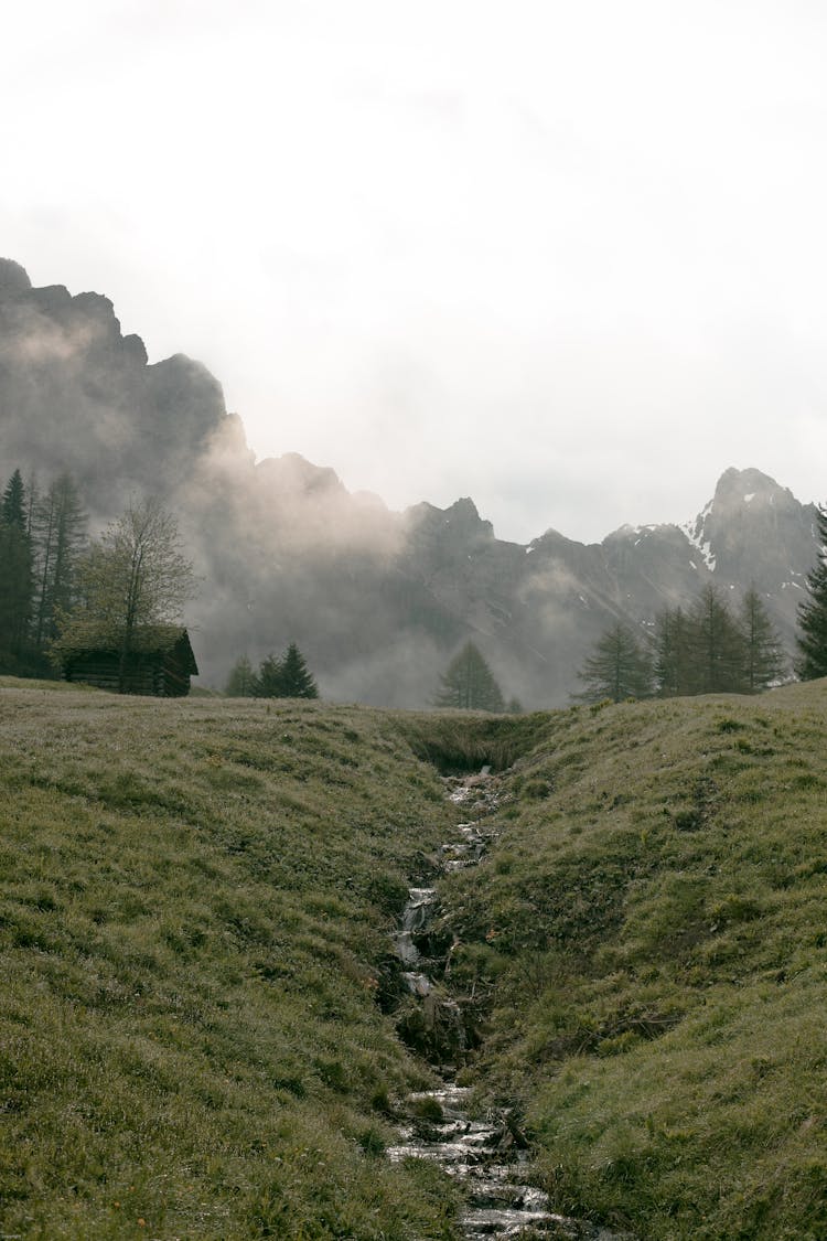 Lonesome House On Foggy Valley Against Massive Mountain Ridge