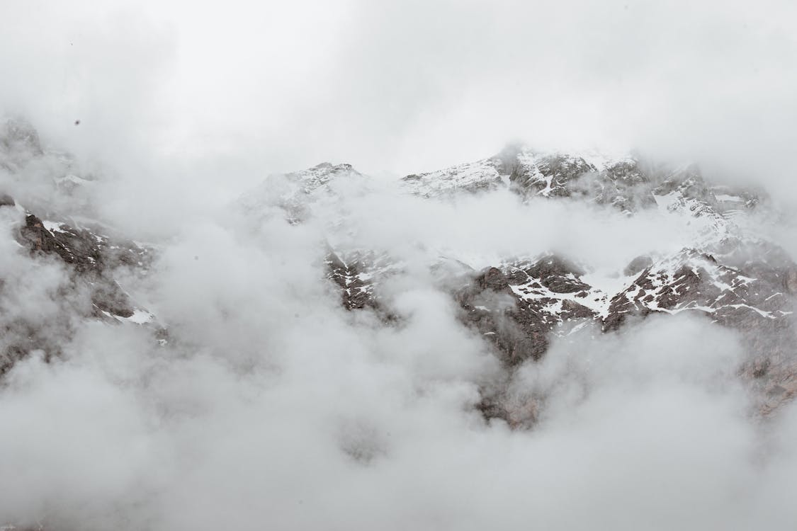 Free Dense fog covering massive mountain range with snowy rocky slopes on overcast day Stock Photo