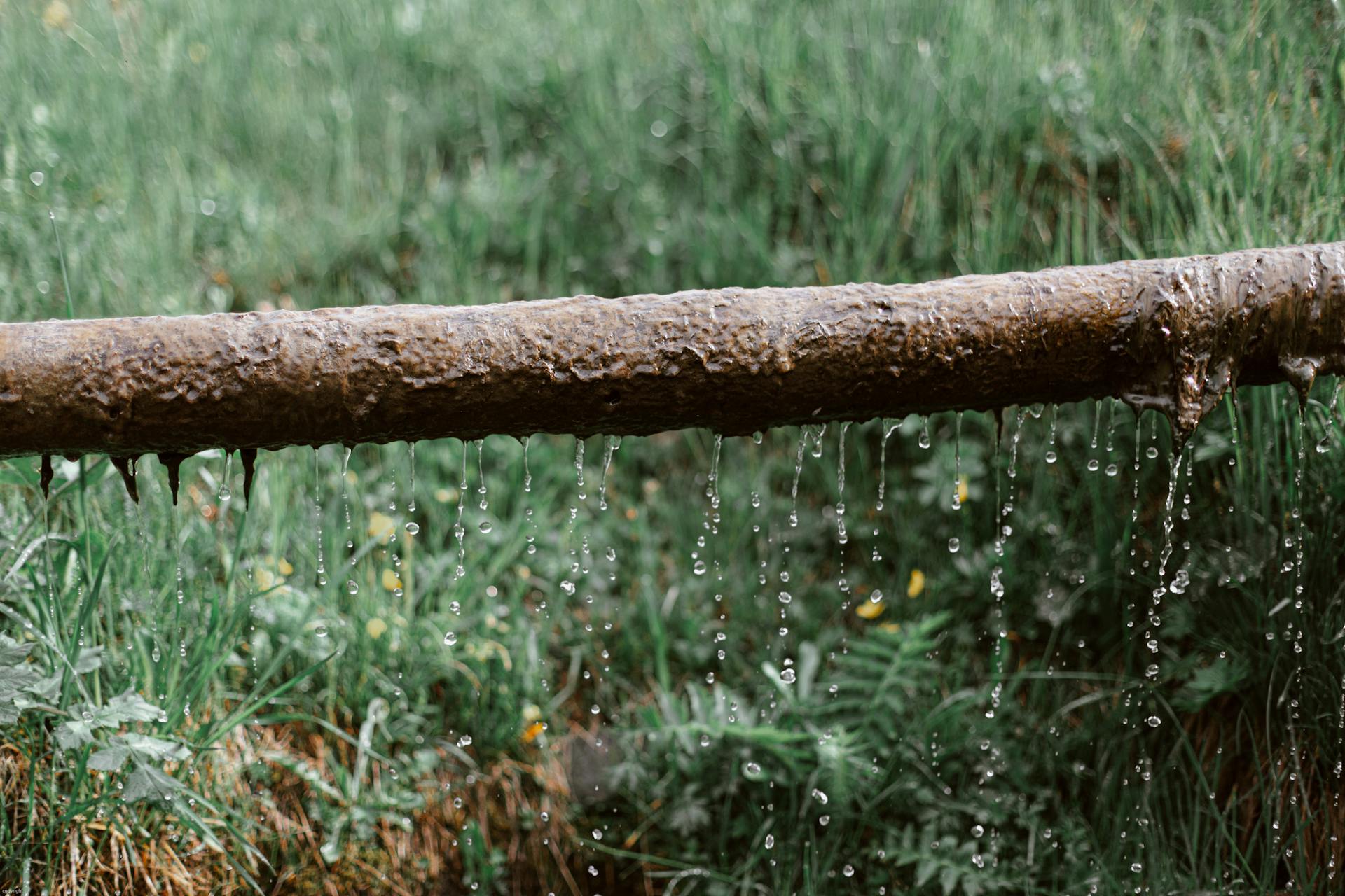 Rusted metal leaking pipe above grassy meadow