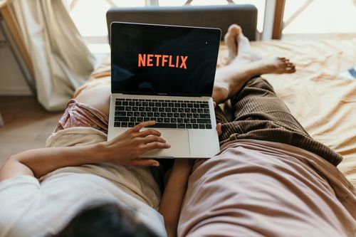 Free A couple lying comfortably in bed watching Netflix on a laptop, enjoying leisure time together indoors. Stock Photo