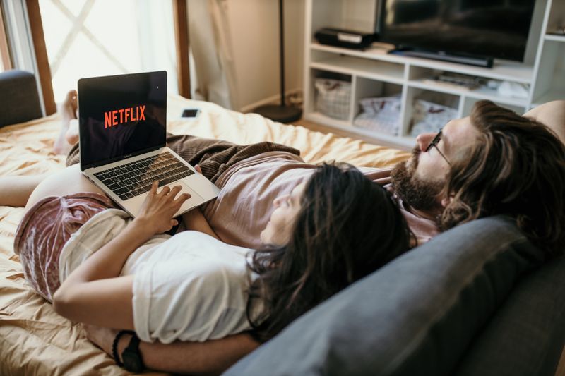 A cozy couple lounging in bed, streaming Netflix together on a laptop, enjoying a peaceful moment.