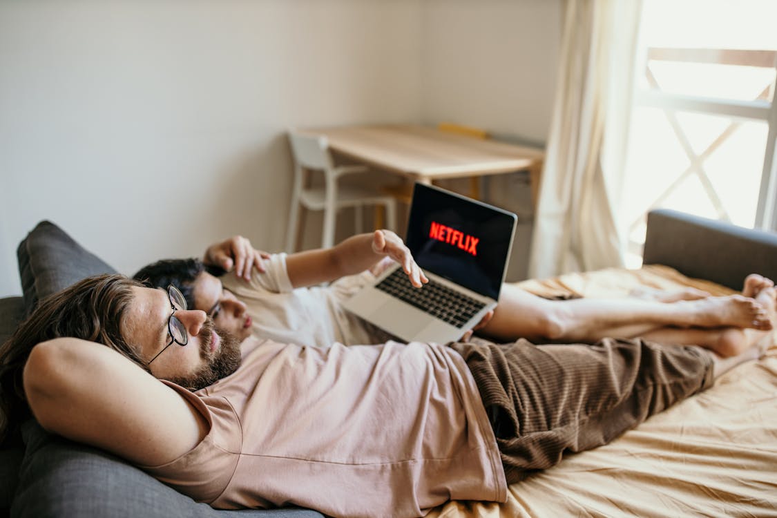 Man in White T-shirt Lying on Bed Using Macbook