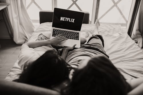 Grayscale Photo of Woman Lying on Bed Using Macbook