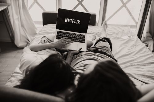Free A couple relaxing together, watching Netflix on a laptop in a cozy bedroom setting. Stock Photo