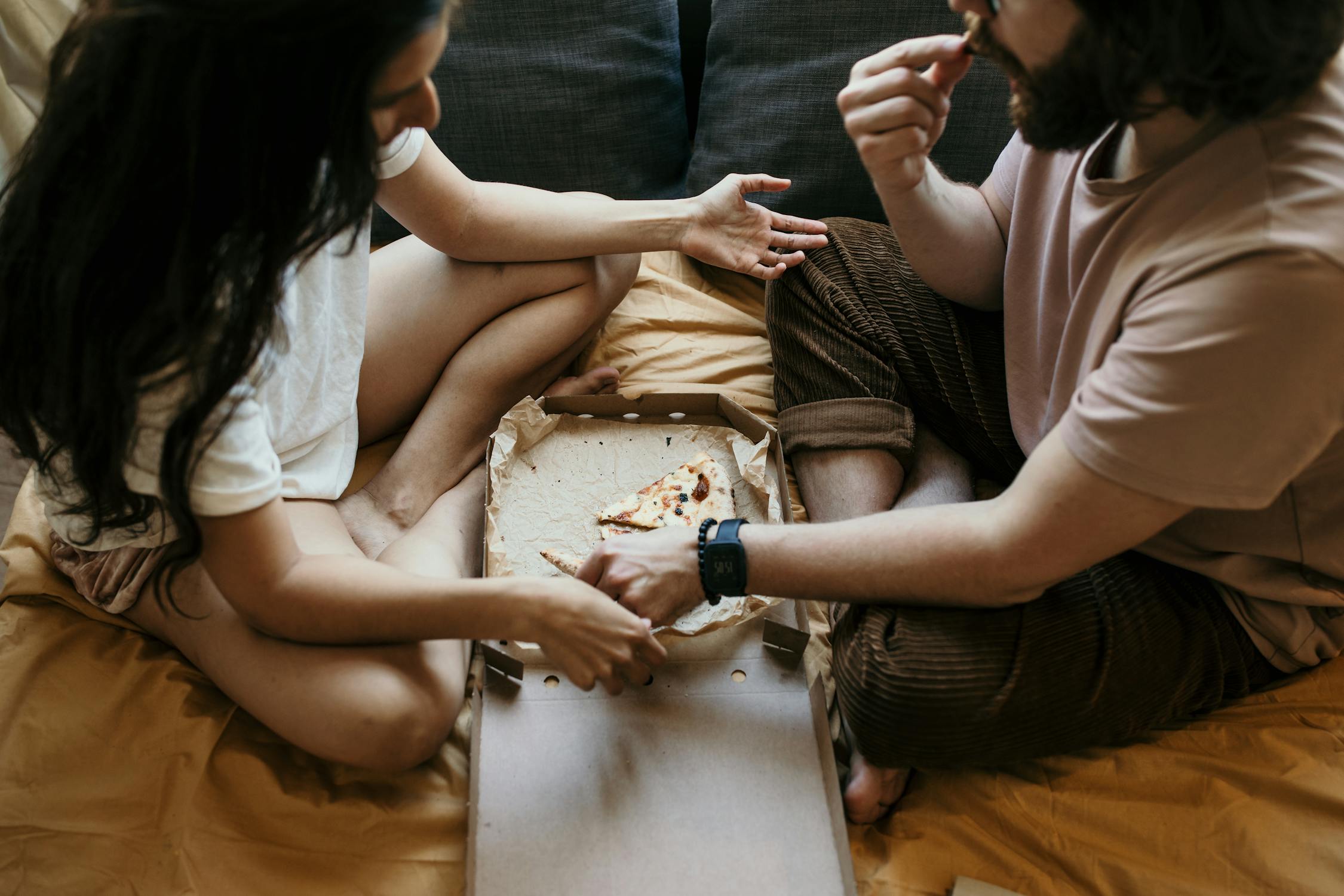 Order some pizza for your spa day at home A couple eating pizza together on bed