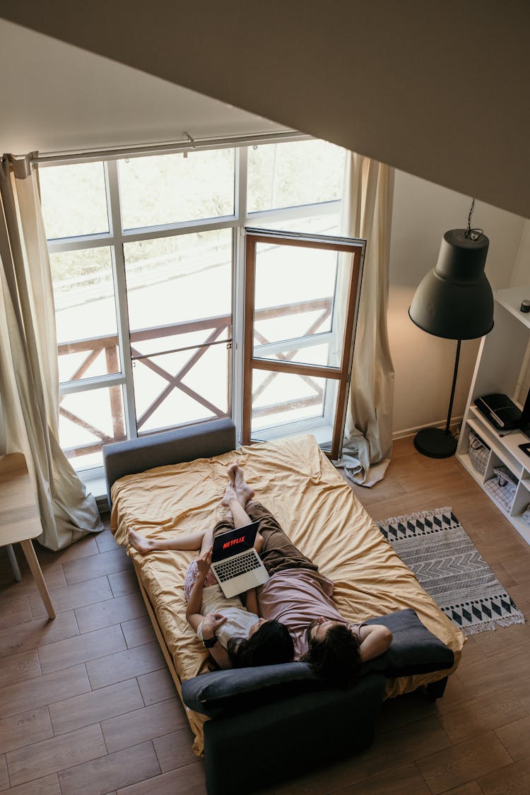 A Couple Lying On Bed Watching On Laptop
