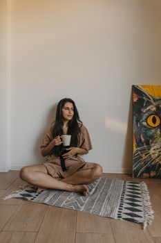 一位年轻女子坐在室内，靠近当代艺术，喝着咖啡放松，散发着平静和宁静