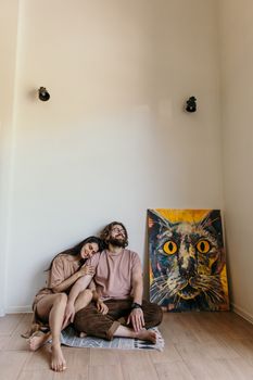 一对夫妇坐在极简主义的房间里，旁边挂着一幅充满活力的猫画，共同享受着宁静的时刻