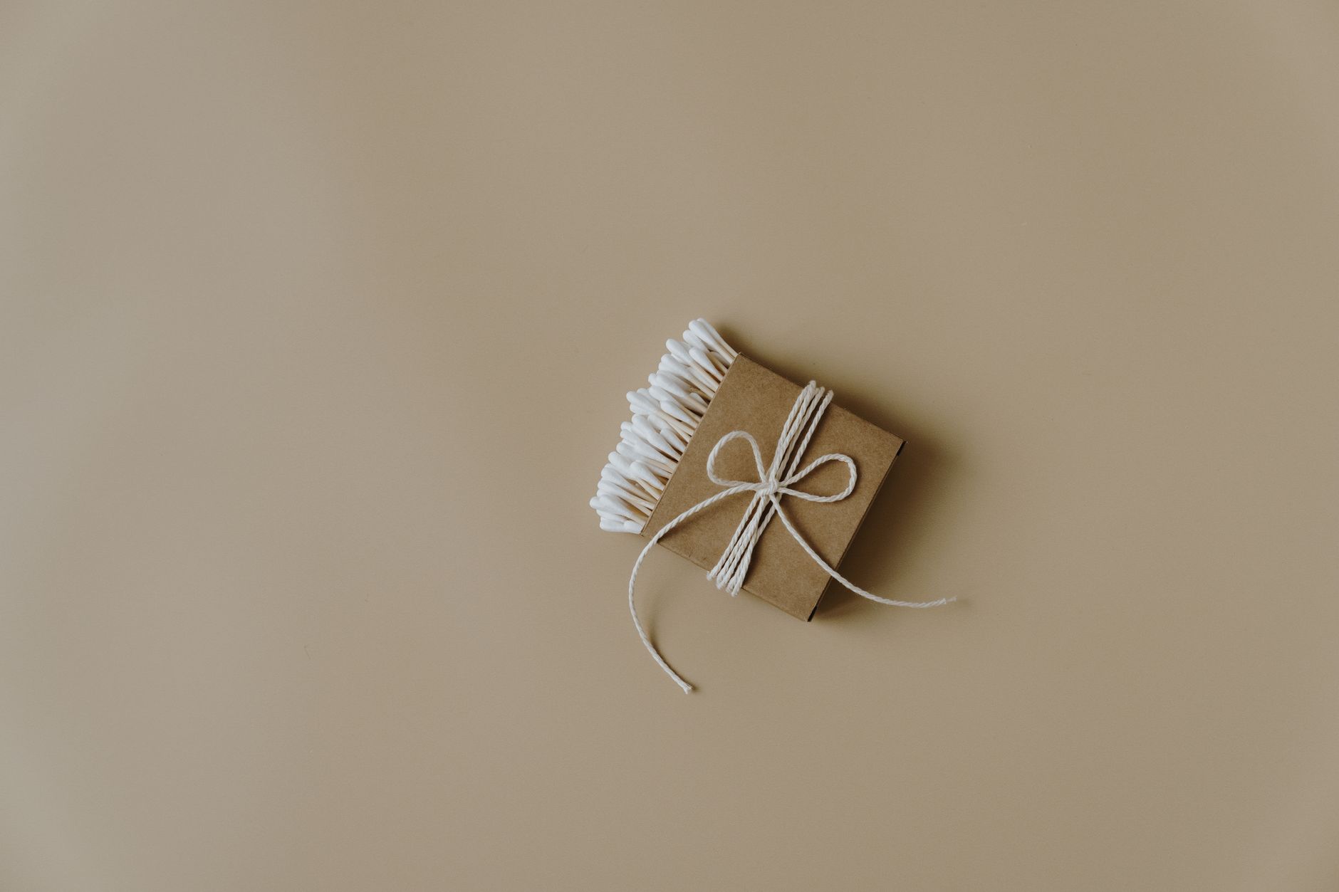 Minimalist design featuring eco-friendly cotton buds wrapped in brown paper on neutral background.