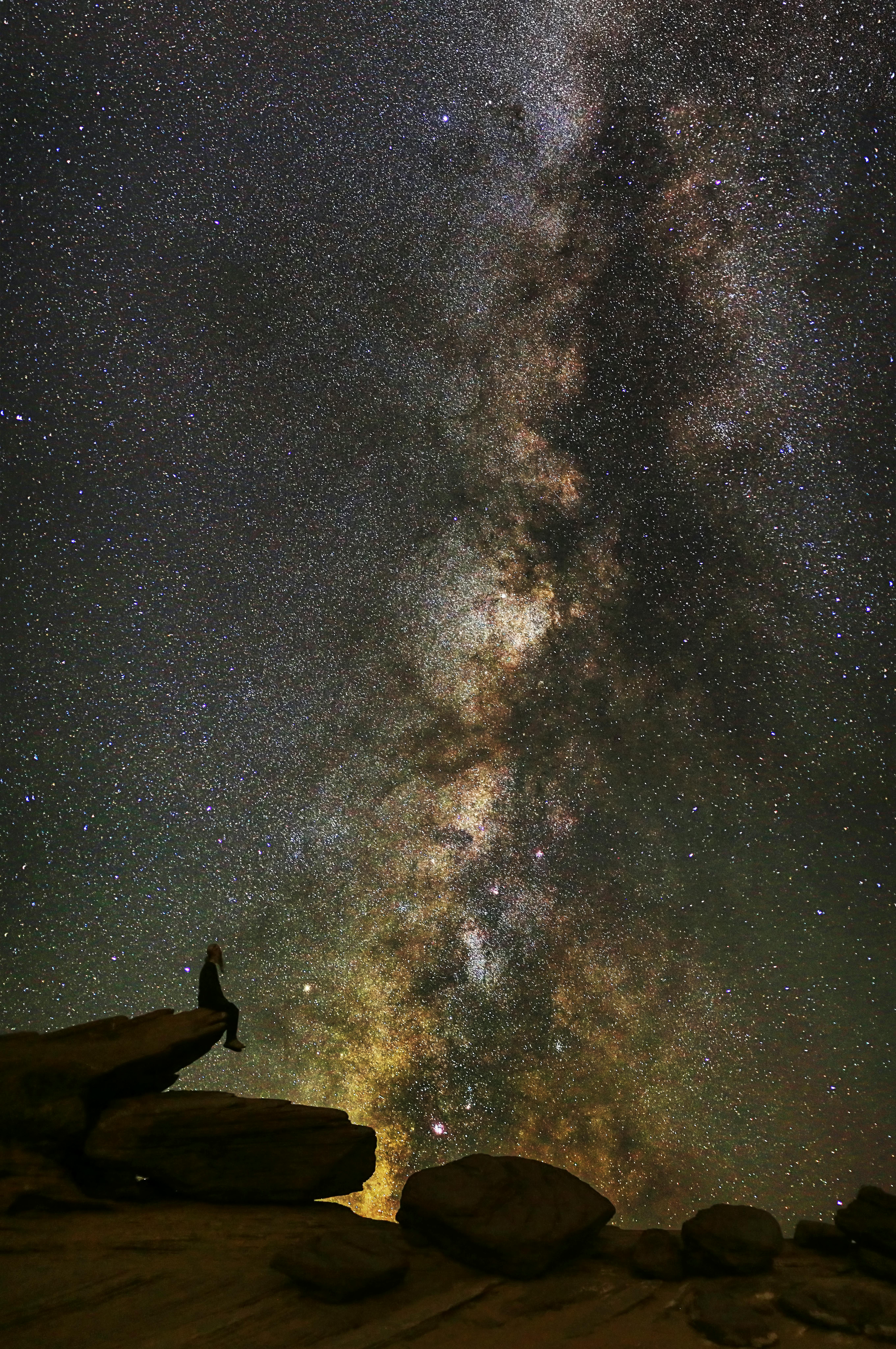 man in black jacket standing on rock formation under starry night