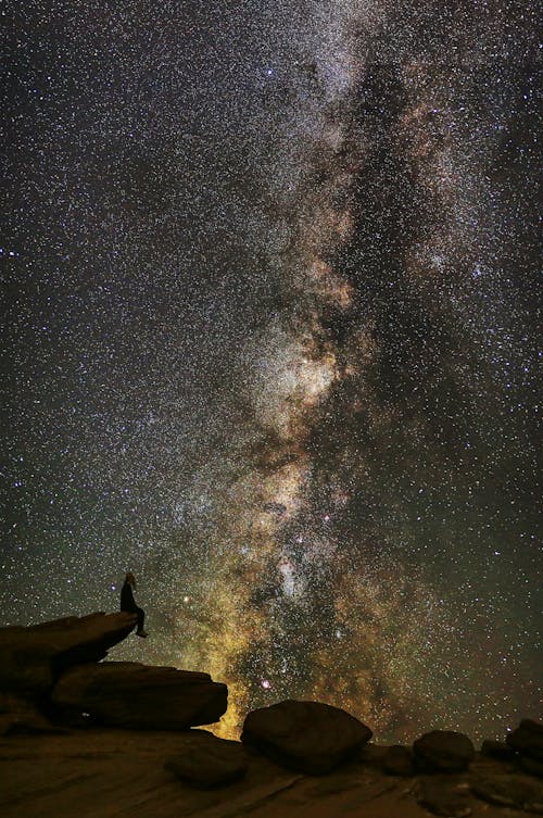 Free Man in Black Jacket Standing on Rock Formation Under Starry Night Stock Photo