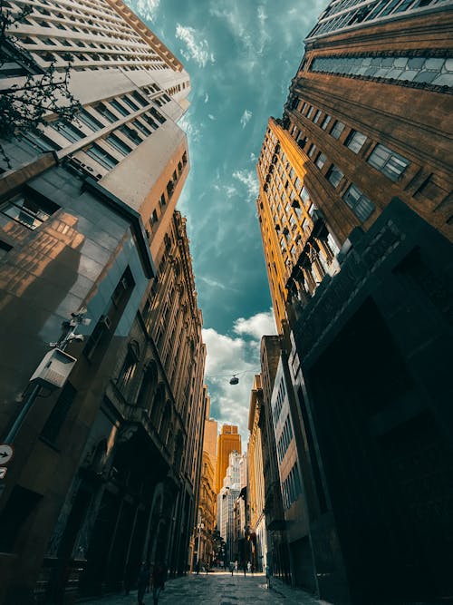 From below of narrow street between tall contemporary skyscrapers in city downtown against cloudy blue sky