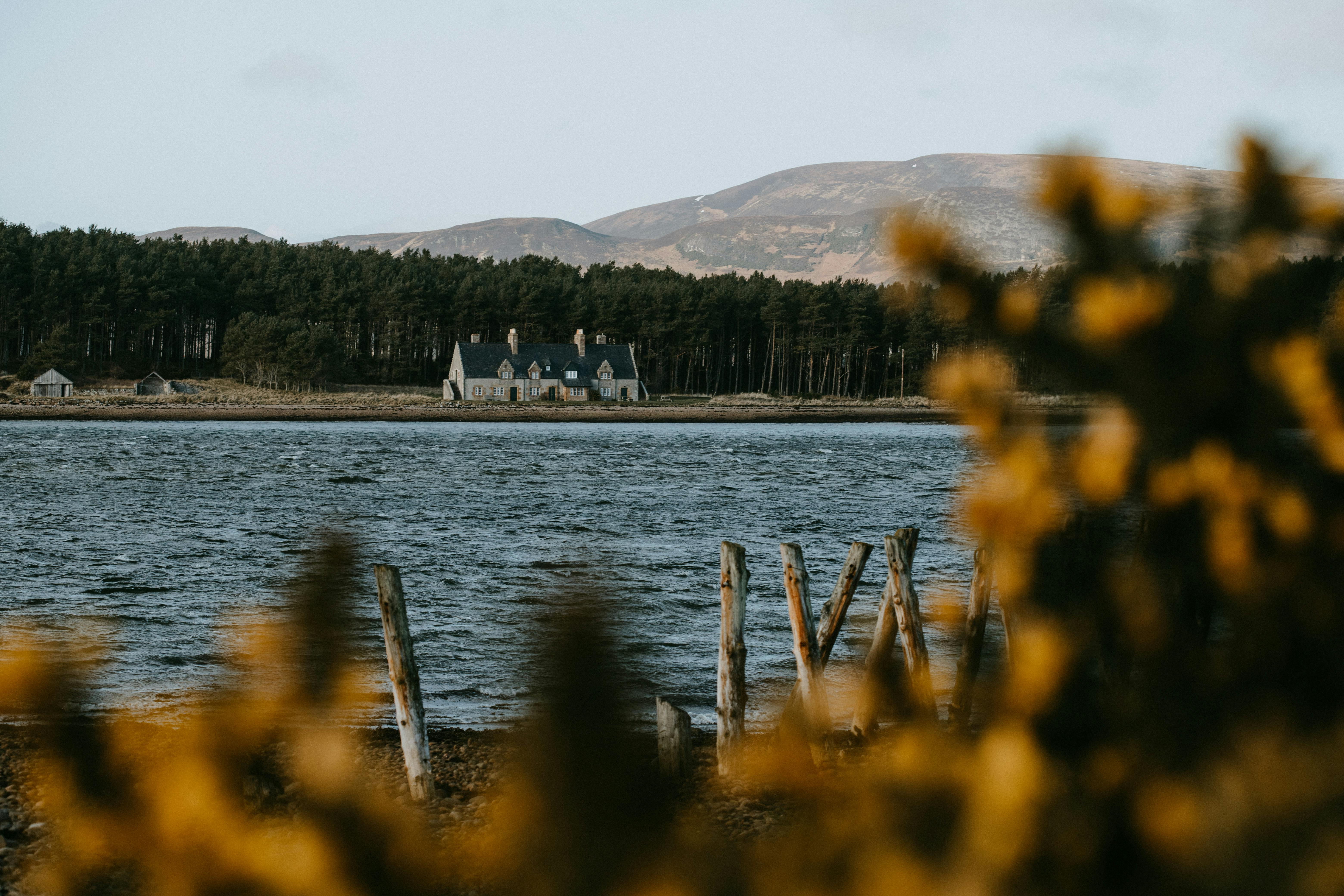Idyllic scene of a house by a lake with mountains and forest in Scotland at sunset.