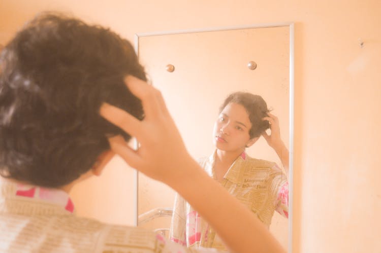 Pensive Young Ethnic Teen Looking In Mirror