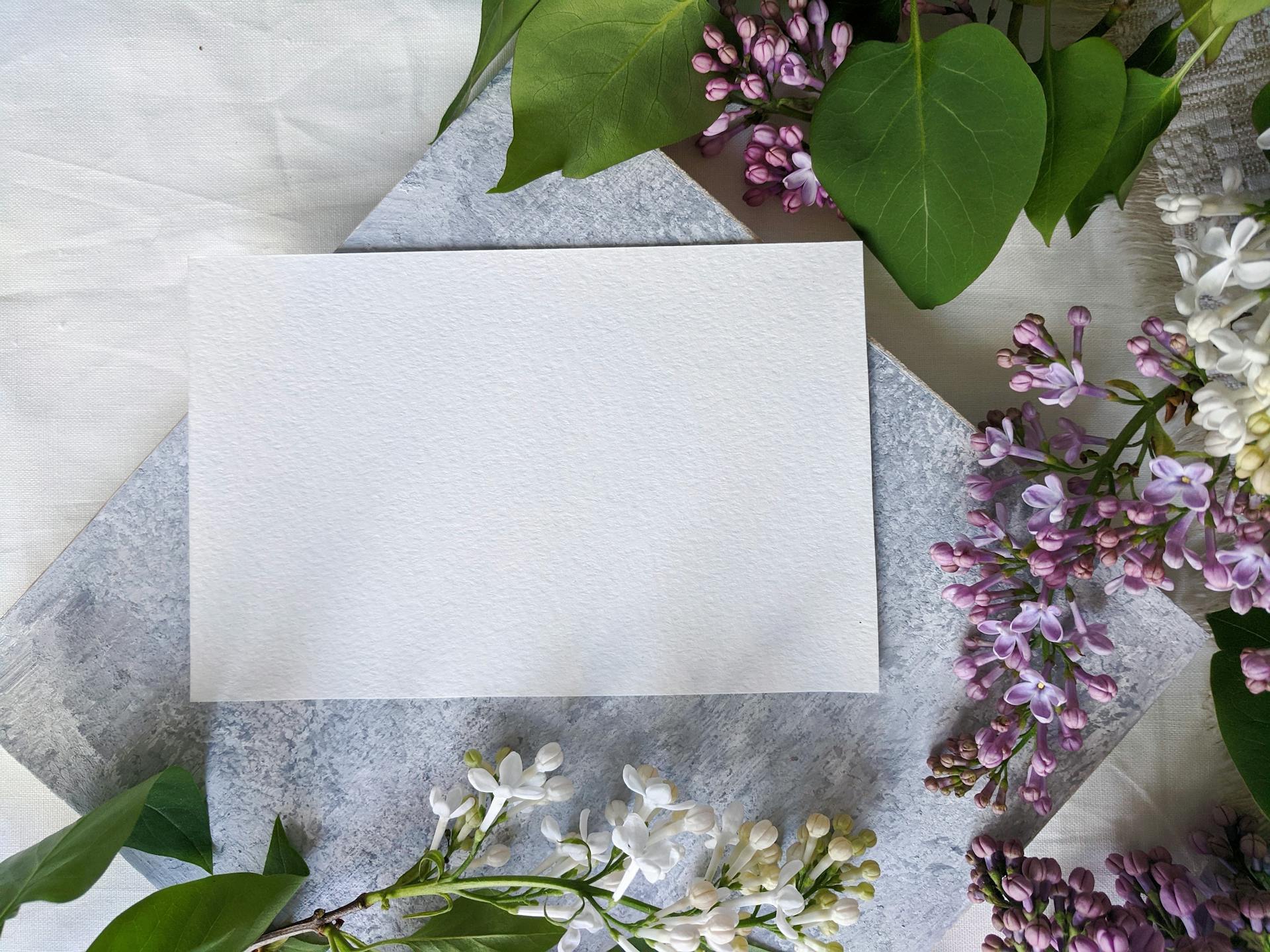 Flat lay of a blank card surrounded by lilac flowers and green leaves, perfect for spring greetings or invitations.
