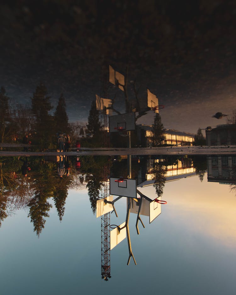 A Reflection Of People Near Basketball Hoops On Body Of Water 