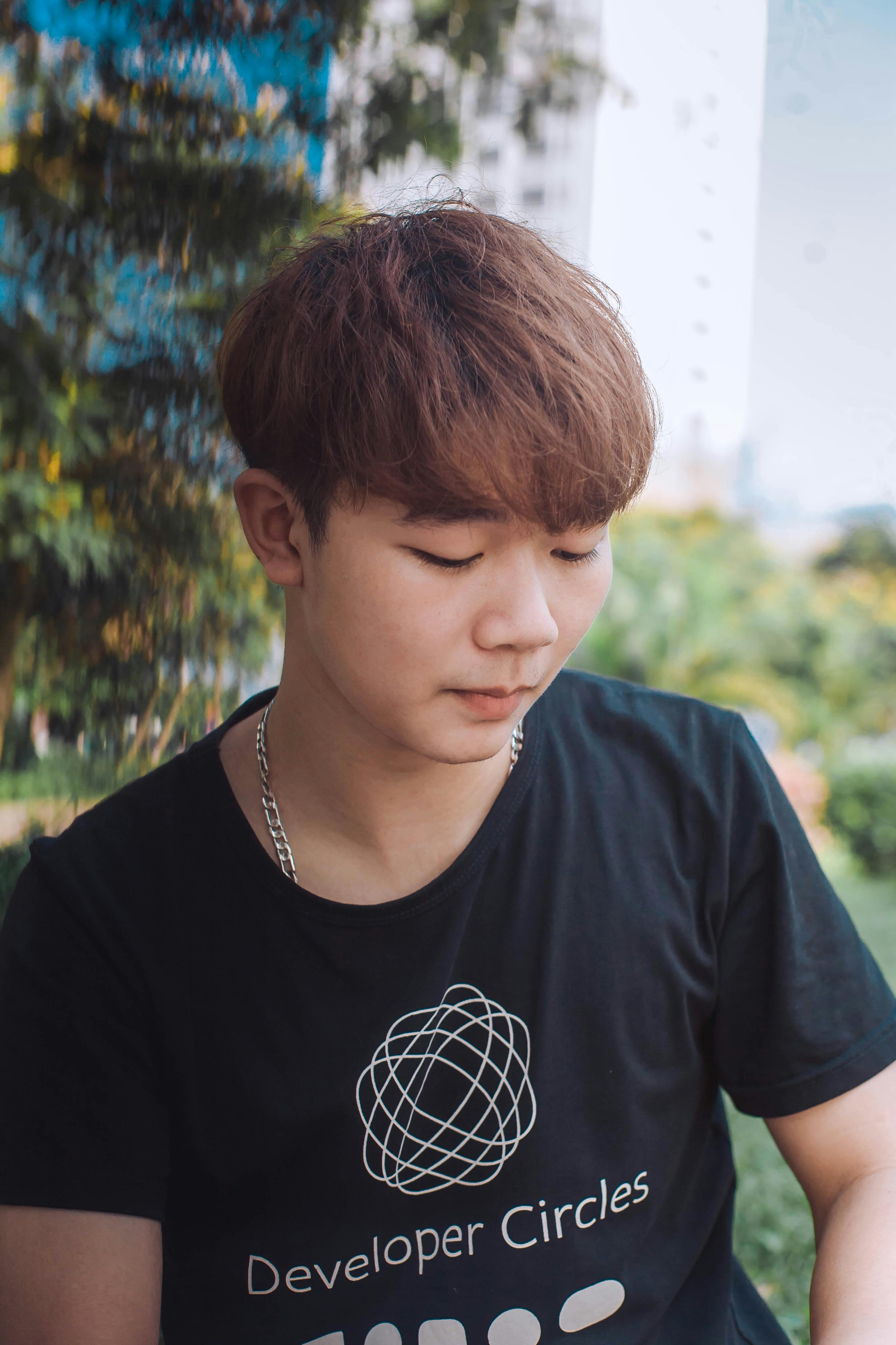 Casual portrait of a young man looking down, set in an outdoor green environment.
