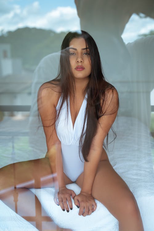 Young woman in white bodysuit sitting on bed