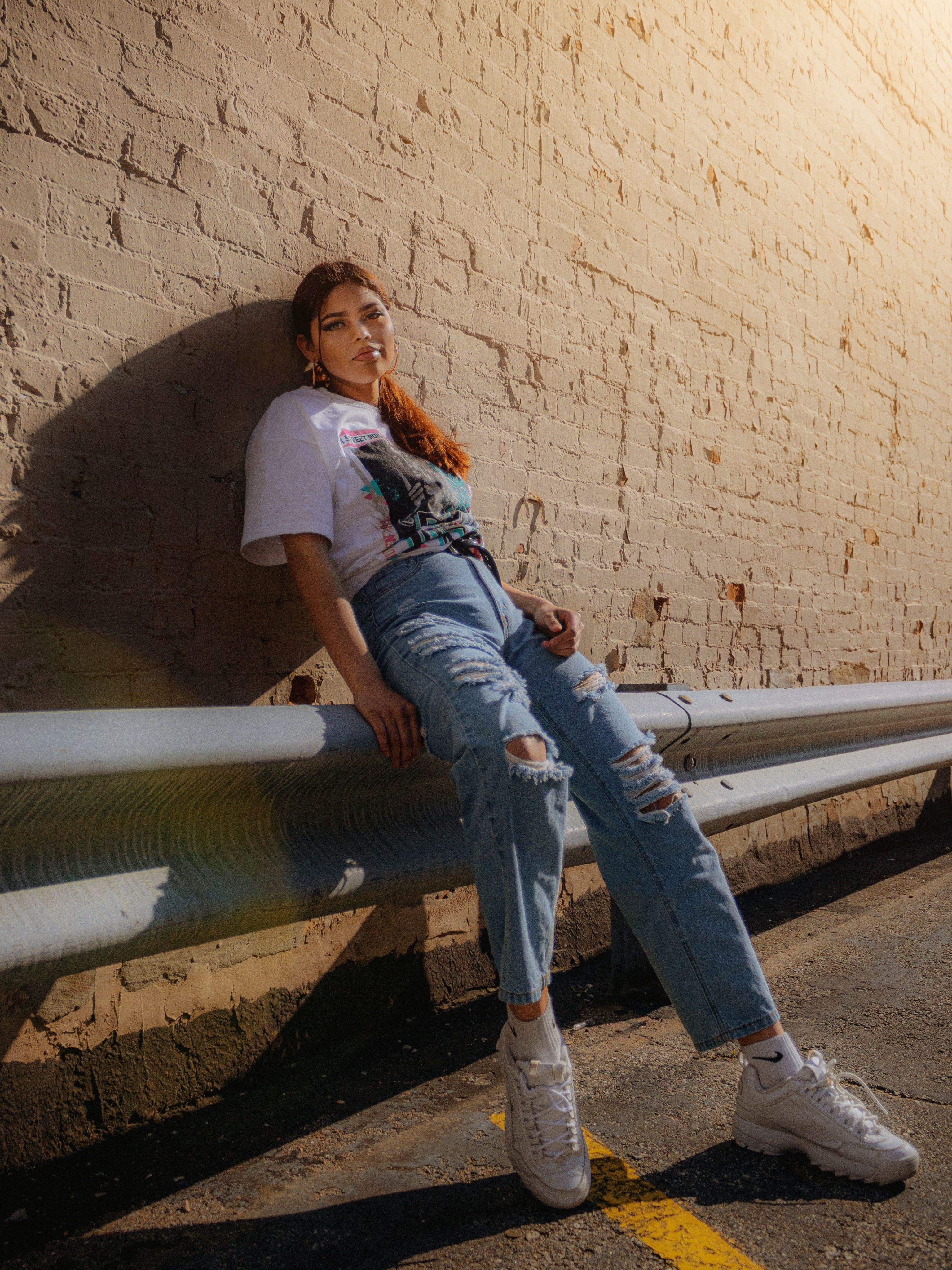 A Woman in Denim Ripped Jeans and White T-shirt Sitting on Barrier ...