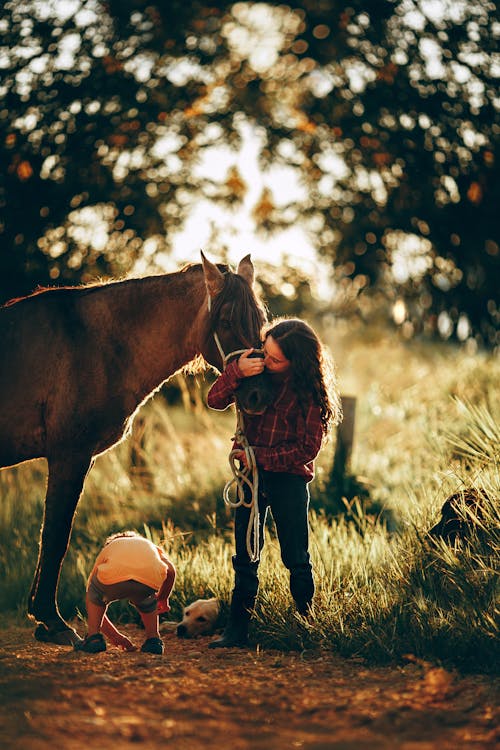 Full length of teen girl embracing horse standing on grassy ground with little kid and dog