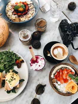 Aerial shot of brunch dishes, drinks, and camera on a marble table, creating a vibrant and inviting scene.