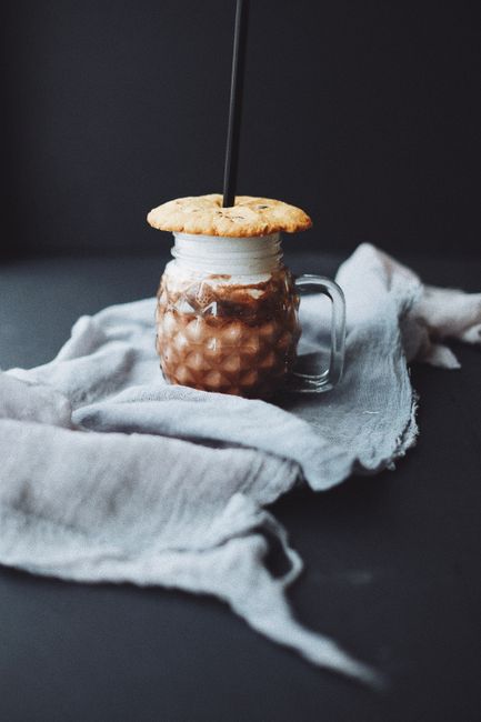 Coffee drink in pineapple shaped glass with cookie cap on gray cloth placed against black background