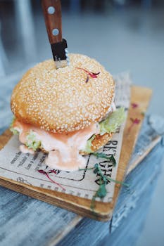 High angle of appetizing burger with meat patty sauce and sesame seeds served on wooden board with knife