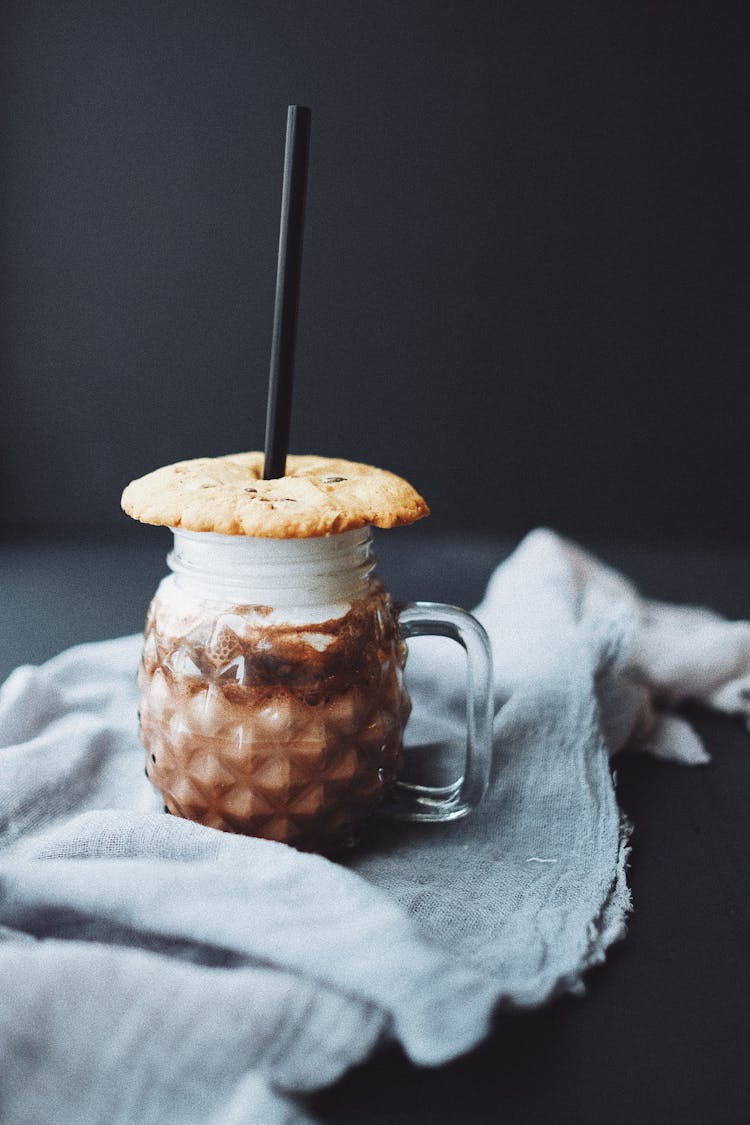 Iced Coffee In Unusual Glass With Cookie And Straw On Black Surface