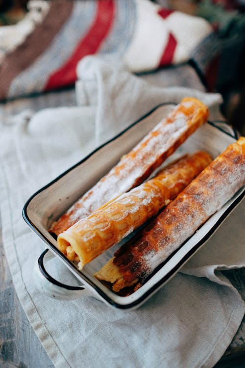 Free From above of crispy waffle rolls with sweet filling and powdered sugar in enameled baking dish placed on rustic wooden table Stock Photo
