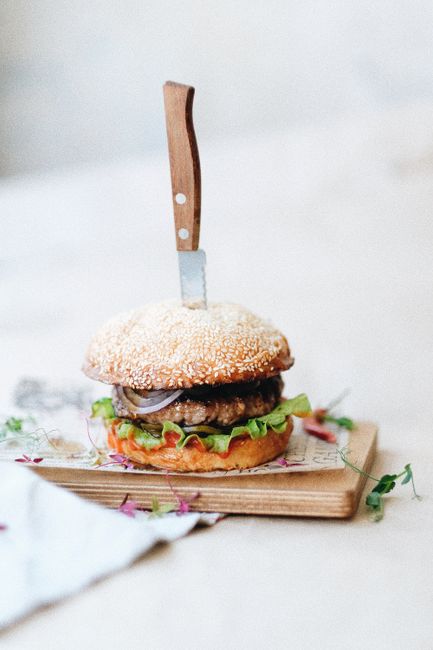 Yummy fresh hamburger with meat patty onion and lettuce placed on wooden cutting board and served with knife