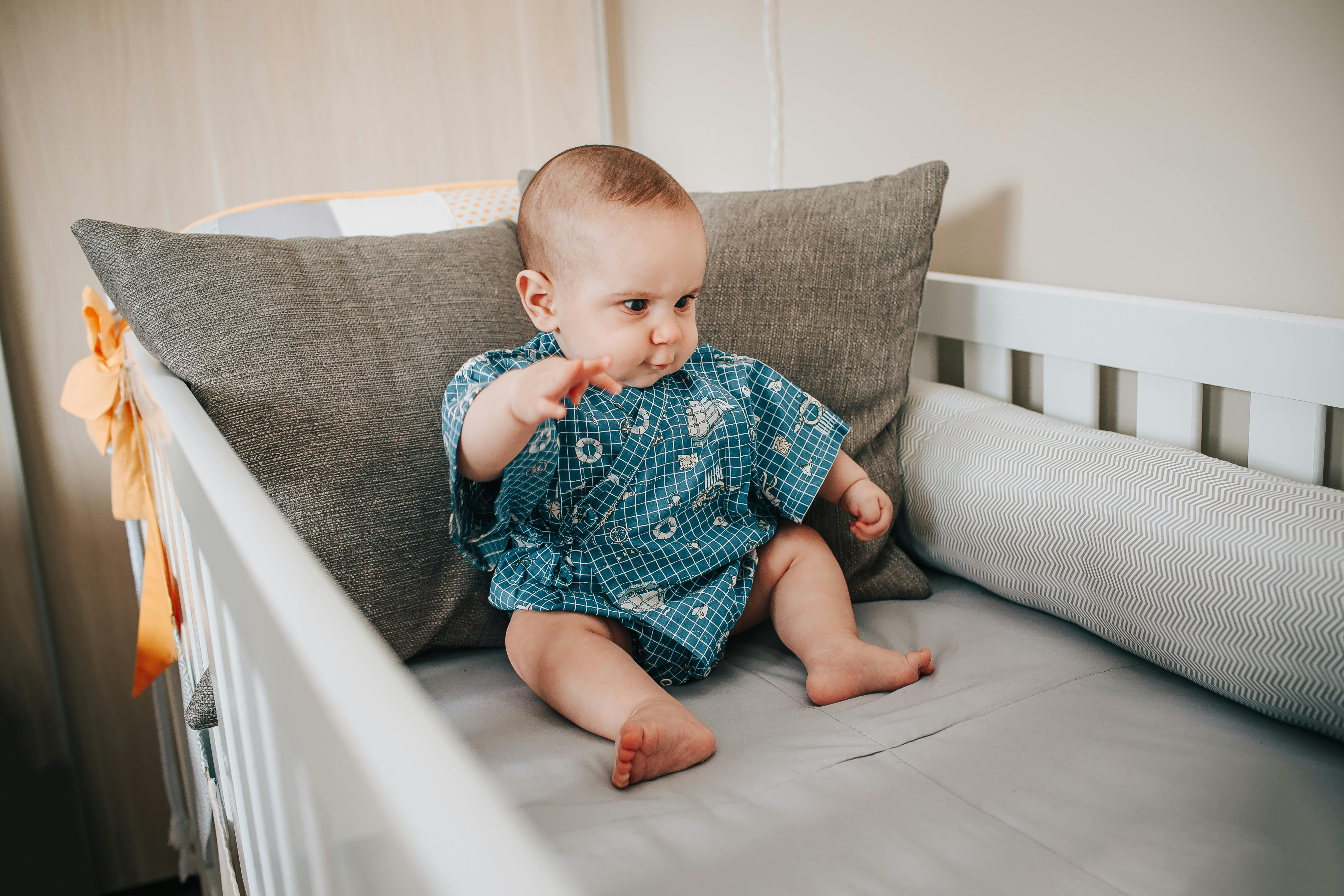 Full body of adorable little child sitting on gray blanket and looking down