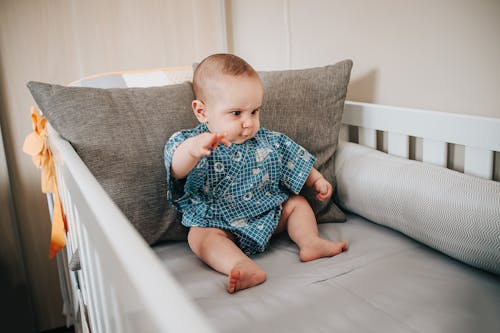 Free Full body of adorable little child sitting on gray blanket and looking down Stock Photo
