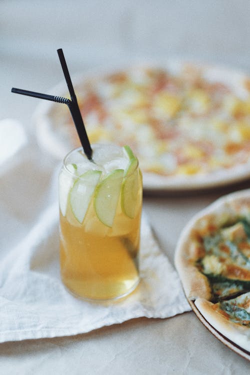 Cold fresh drink in glass with straws near pizza on table