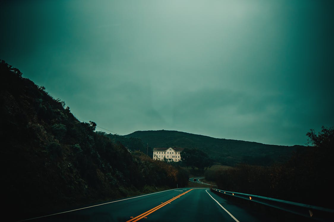 Empty highway through hilly green terrain with big white mansion