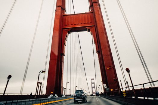 Cars riding along asphalt surface of famous Golden Gate Bridge in San Francisco on cloudy overcast day